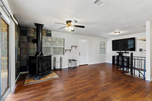 living room with visible vents, a wood stove, ceiling fan, a textured ceiling, and wood finished floors