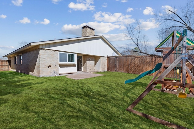 back of house featuring a lawn, a fenced backyard, a chimney, a playground, and brick siding