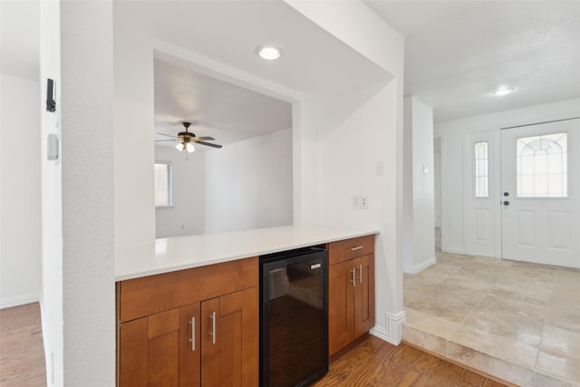 kitchen featuring beverage cooler, baseboards, light countertops, light wood-type flooring, and brown cabinets