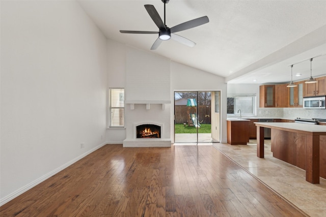 unfurnished living room featuring light wood finished floors, vaulted ceiling, ceiling fan, a lit fireplace, and baseboards