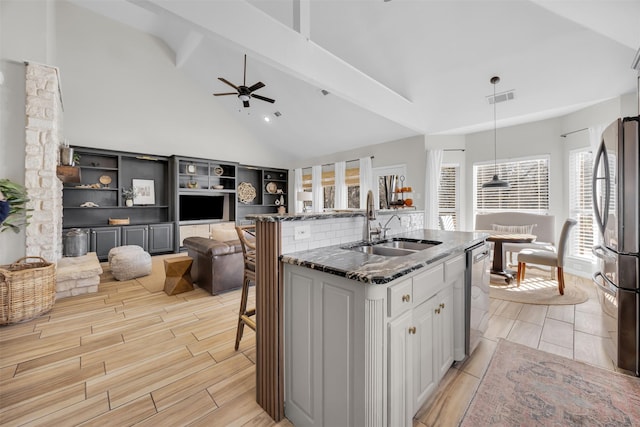 kitchen featuring visible vents, dark stone countertops, a sink, stainless steel appliances, and beam ceiling