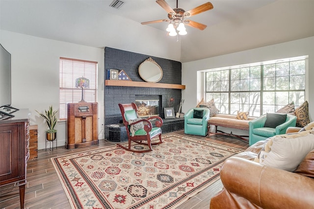 living area with visible vents, a brick fireplace, ceiling fan, vaulted ceiling, and wood finished floors