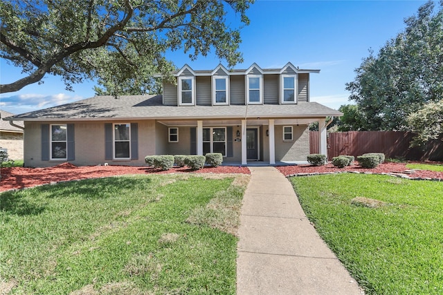 view of front of home with a shingled roof, covered porch, fence, and a front lawn