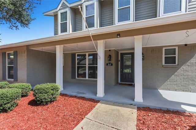 doorway to property featuring covered porch and brick siding