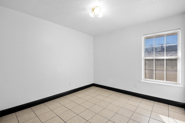 unfurnished room featuring a textured ceiling, light tile patterned floors, and baseboards