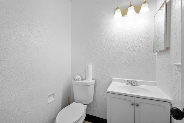 half bath featuring toilet, a textured wall, and vanity