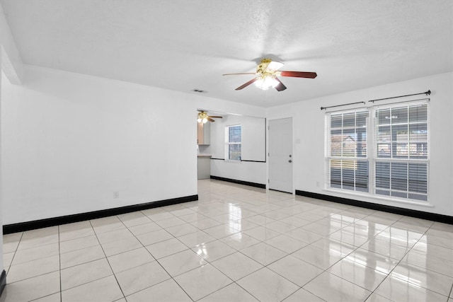 unfurnished room with a textured ceiling, light tile patterned flooring, visible vents, baseboards, and a ceiling fan