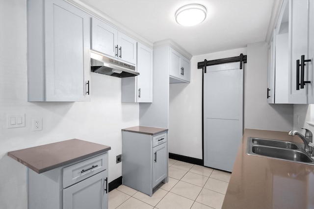 kitchen with light tile patterned floors, a barn door, dark countertops, under cabinet range hood, and a sink