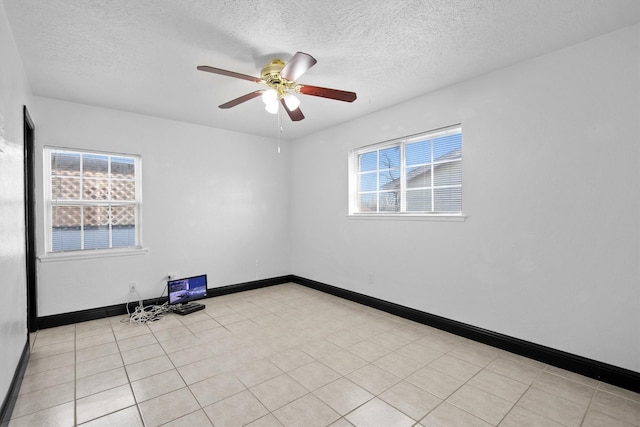 empty room featuring light tile patterned floors, a textured ceiling, baseboards, and a ceiling fan