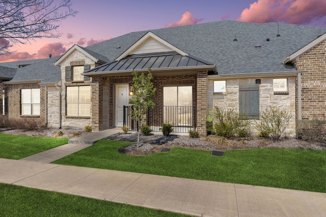 view of front of house with stone siding, metal roof, roof with shingles, a standing seam roof, and brick siding