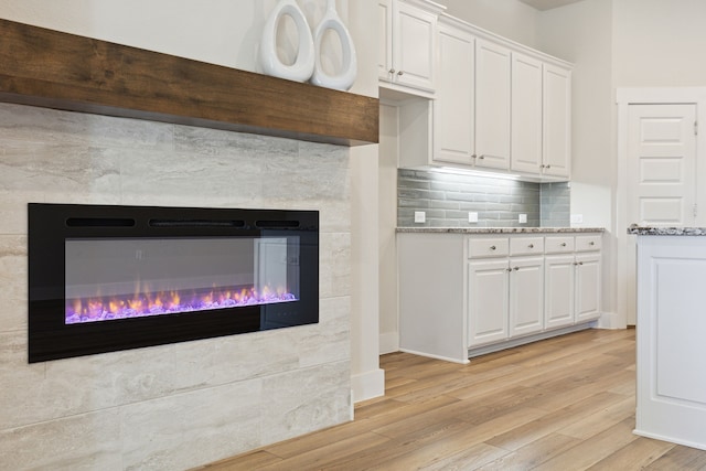 3830 Dalea Dr, Prosper, TX 75078 - kitchen featuring light wood finished floors, tasteful backsplash, white cabinets, a glass covered fireplace, and light stone counters