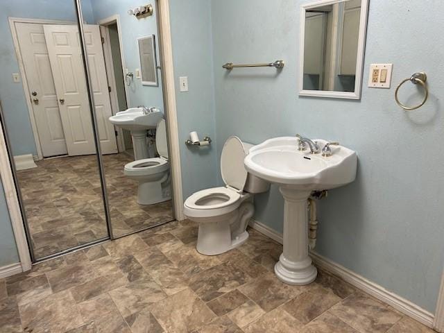 bathroom featuring stone finish floor, toilet, and baseboards