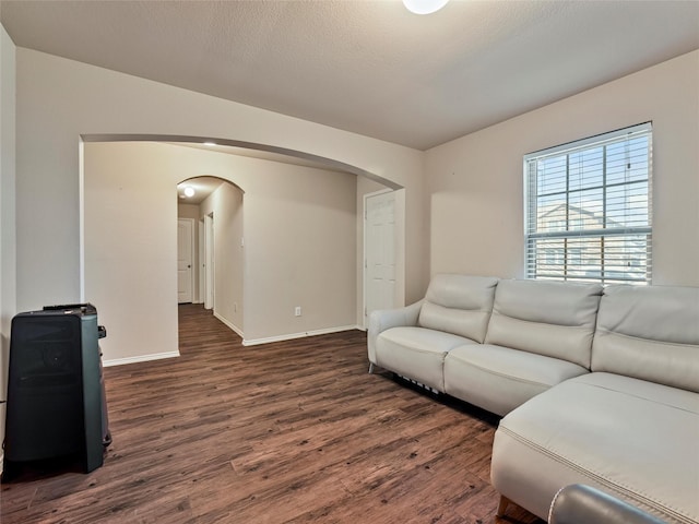 living room featuring baseboards, a textured ceiling, arched walkways, and dark wood-type flooring