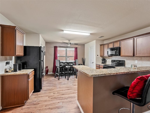 kitchen with visible vents, light wood-style flooring, backsplash, a peninsula, and black appliances