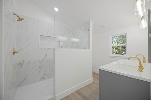 bathroom featuring lofted ceiling, wood finished floors, vanity, baseboards, and a marble finish shower