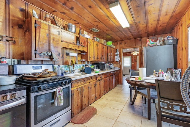 kitchen featuring light tile patterned floors, wooden walls, a sink, wood ceiling, and appliances with stainless steel finishes