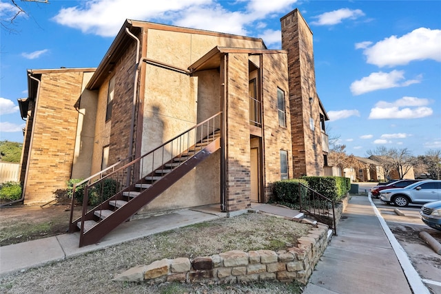 view of property exterior with a chimney, brick siding, and stairway