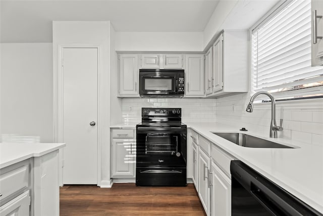 kitchen featuring dark wood finished floors, light countertops, a sink, and black appliances