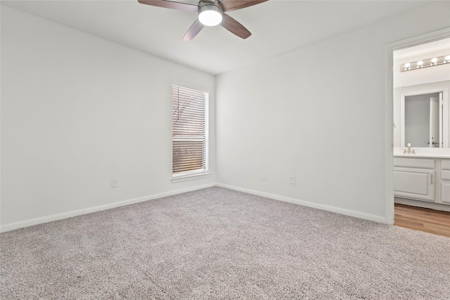 unfurnished bedroom featuring light carpet, baseboards, ceiling fan, ensuite bathroom, and a sink