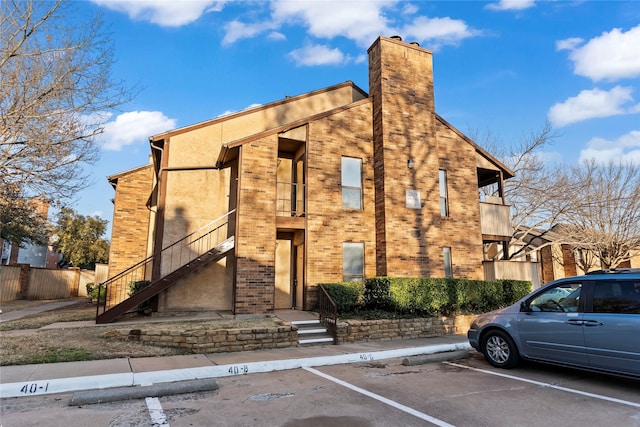 view of front of property featuring brick siding, stairs, stucco siding, uncovered parking, and a chimney