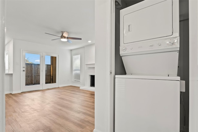 washroom with baseboards, stacked washer and clothes dryer, ceiling fan, light wood-style floors, and a fireplace