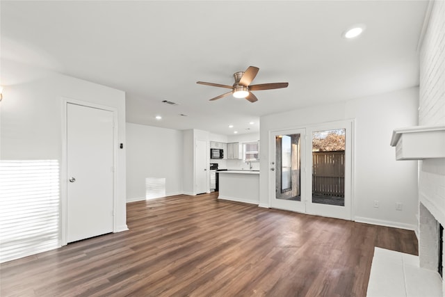 unfurnished living room featuring ceiling fan, a fireplace, visible vents, and dark wood-style flooring