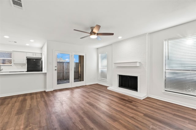 unfurnished living room with visible vents, dark wood-type flooring, a ceiling fan, a brick fireplace, and baseboards