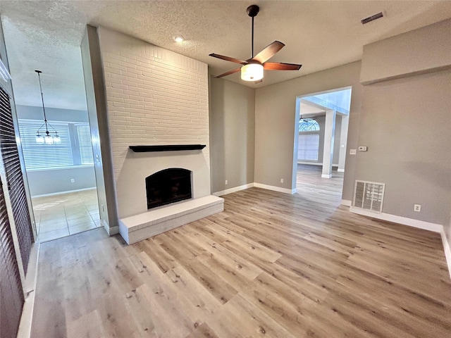 unfurnished living room featuring a textured ceiling, a fireplace, wood finished floors, visible vents, and baseboards