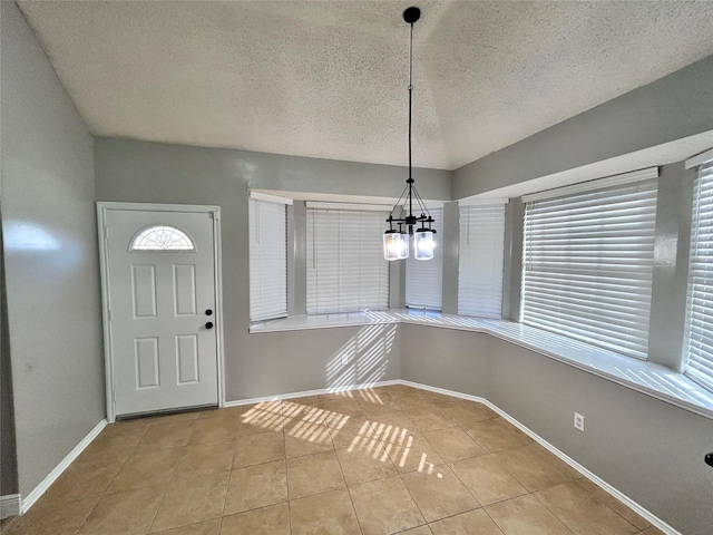 tiled entryway with a notable chandelier, a textured ceiling, baseboards, and a wealth of natural light