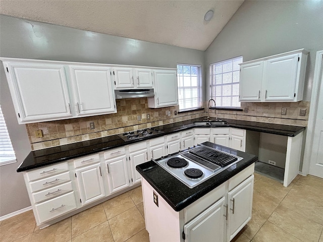 kitchen with stovetop with downdraft, vaulted ceiling, under cabinet range hood, black cooktop, and a sink