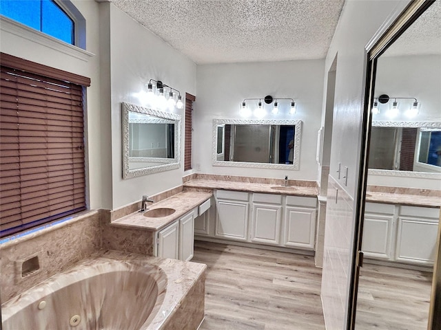 full bathroom featuring a textured ceiling, wood finished floors, a jetted tub, and a sink