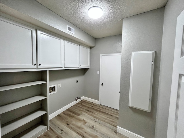 washroom featuring a textured ceiling, hookup for an electric dryer, visible vents, light wood-type flooring, and cabinet space