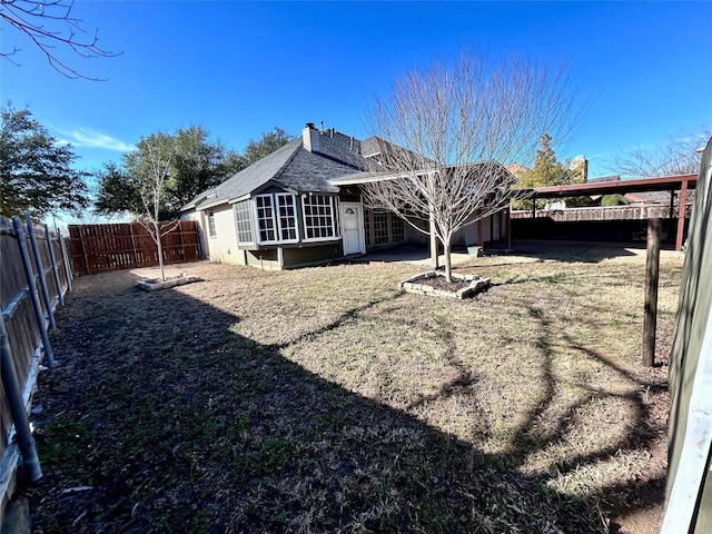 back of property with a shingled roof, a chimney, a fenced backyard, and a lawn