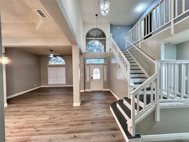 entryway with visible vents, stairway, a high ceiling, wood finished floors, and baseboards