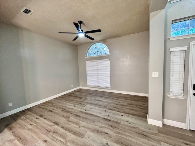 empty room featuring visible vents, a ceiling fan, a textured ceiling, wood finished floors, and baseboards