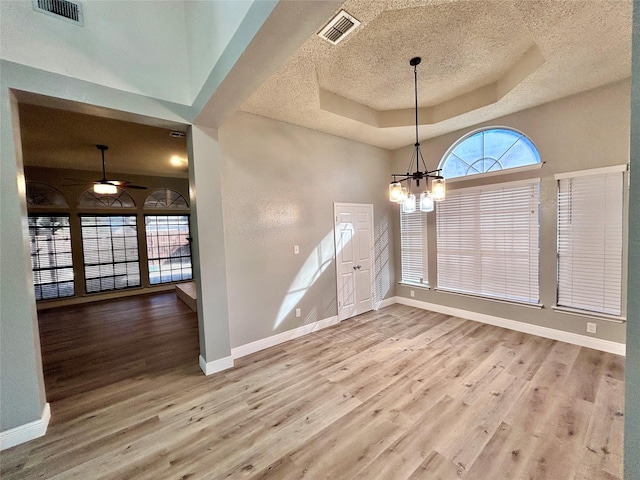 interior space with baseboards, visible vents, a tray ceiling, and wood finished floors