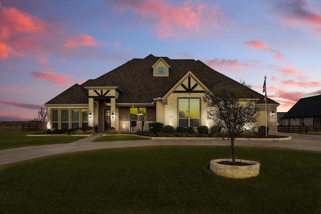 view of front facade with a shingled roof, fence, a front lawn, and brick siding