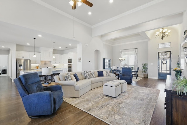 living room with ceiling fan with notable chandelier, a high ceiling, baseboards, dark wood-style floors, and crown molding