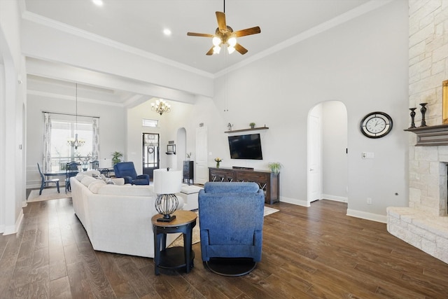 living area featuring arched walkways, a stone fireplace, dark wood-type flooring, baseboards, and crown molding