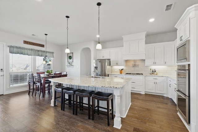 kitchen featuring tasteful backsplash, visible vents, arched walkways, dark wood-style floors, and appliances with stainless steel finishes