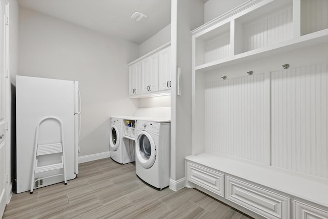 laundry area featuring light wood-type flooring, washing machine and dryer, cabinet space, and baseboards