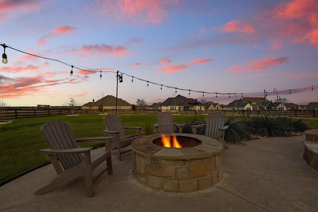 patio terrace at dusk featuring a fire pit, fence, and a yard