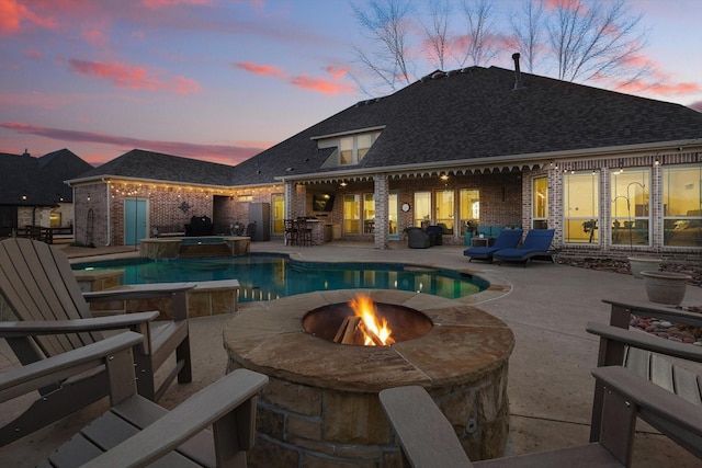 pool at dusk with a patio area, a pool with connected hot tub, and a fire pit