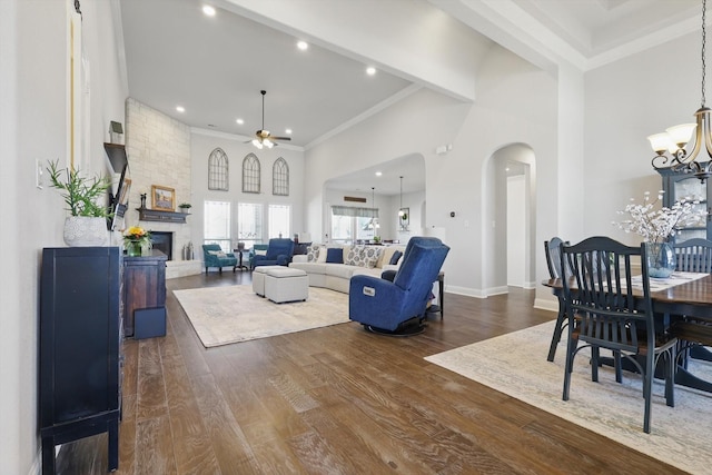 living area with arched walkways, a stone fireplace, ceiling fan with notable chandelier, a high ceiling, and wood finished floors