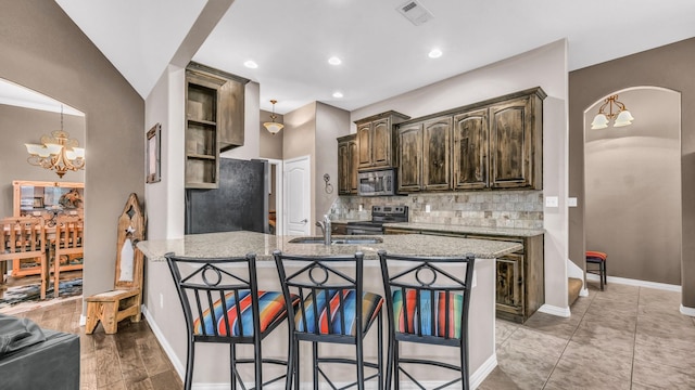 kitchen with arched walkways, visible vents, appliances with stainless steel finishes, dark brown cabinetry, and light stone countertops