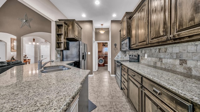 kitchen with light stone counters, arched walkways, stainless steel appliances, backsplash, and a sink