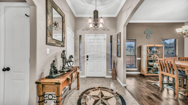 foyer entrance featuring ornamental molding, arched walkways, a notable chandelier, and baseboards