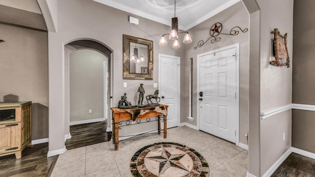 entryway with arched walkways, ornamental molding, light tile patterned flooring, and baseboards