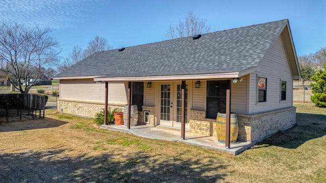 back of property with french doors, stone siding, roof with shingles, a yard, and brick siding