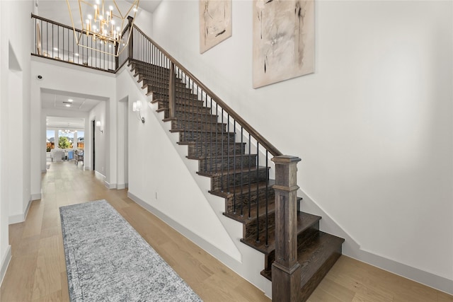 stairway with a chandelier, wood finished floors, a towering ceiling, and baseboards